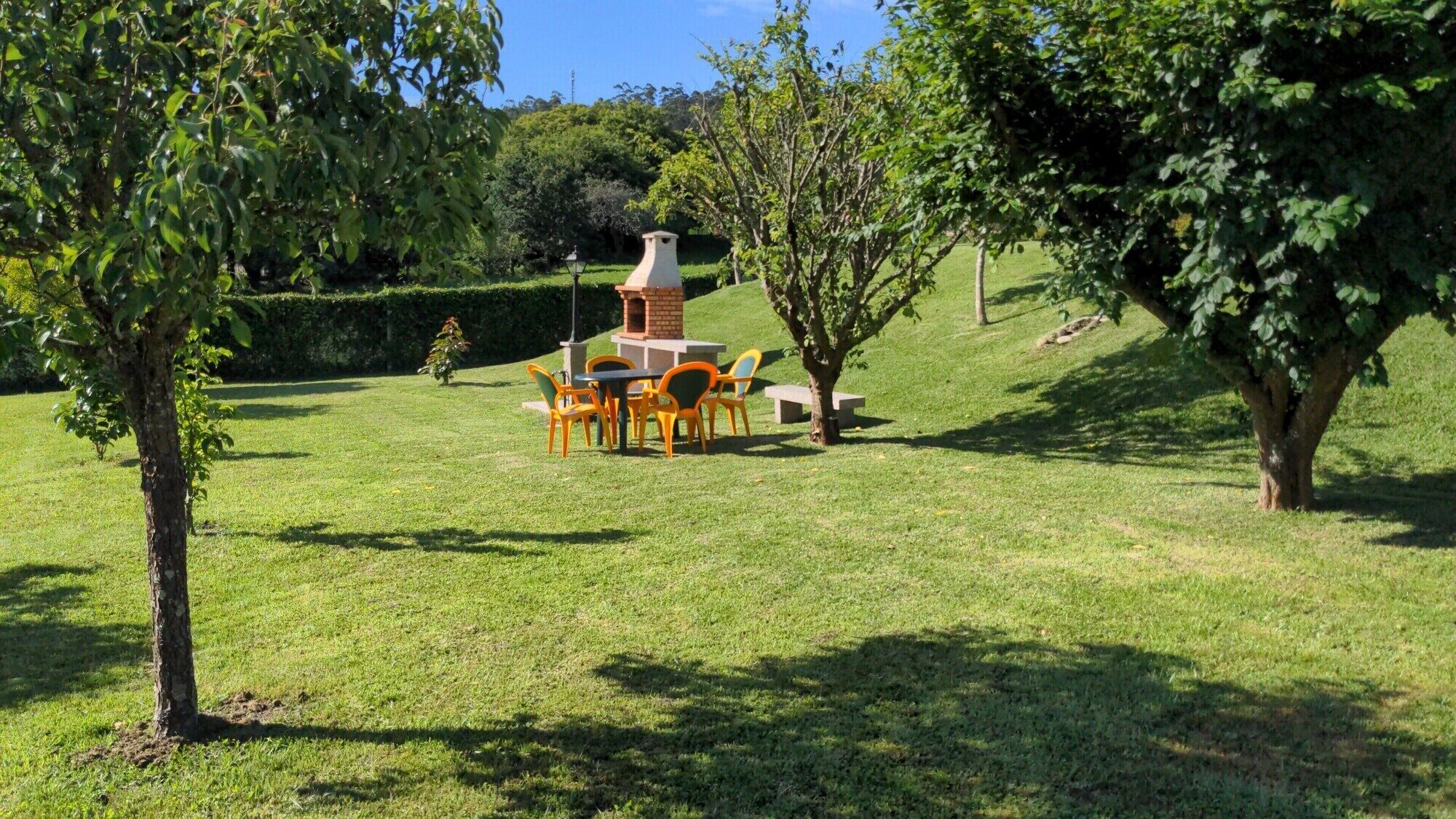 Een gazon met een buitenruimte met een bakstenen constructie, mogelijk een barbecue, omringd door stoelen en tafels.