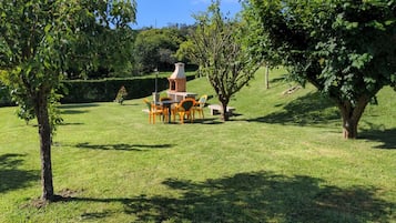 Een gazon met een buitenruimte met een bakstenen constructie, mogelijk een barbecue, omringd door stoelen en tafels.