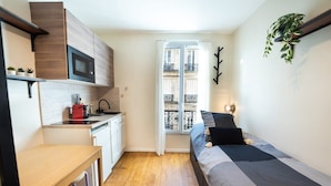 Une chambre compacte comprenant un lit, un petit bureau, un four à micro-ondes et une fenêtre donnant sur un balcon.