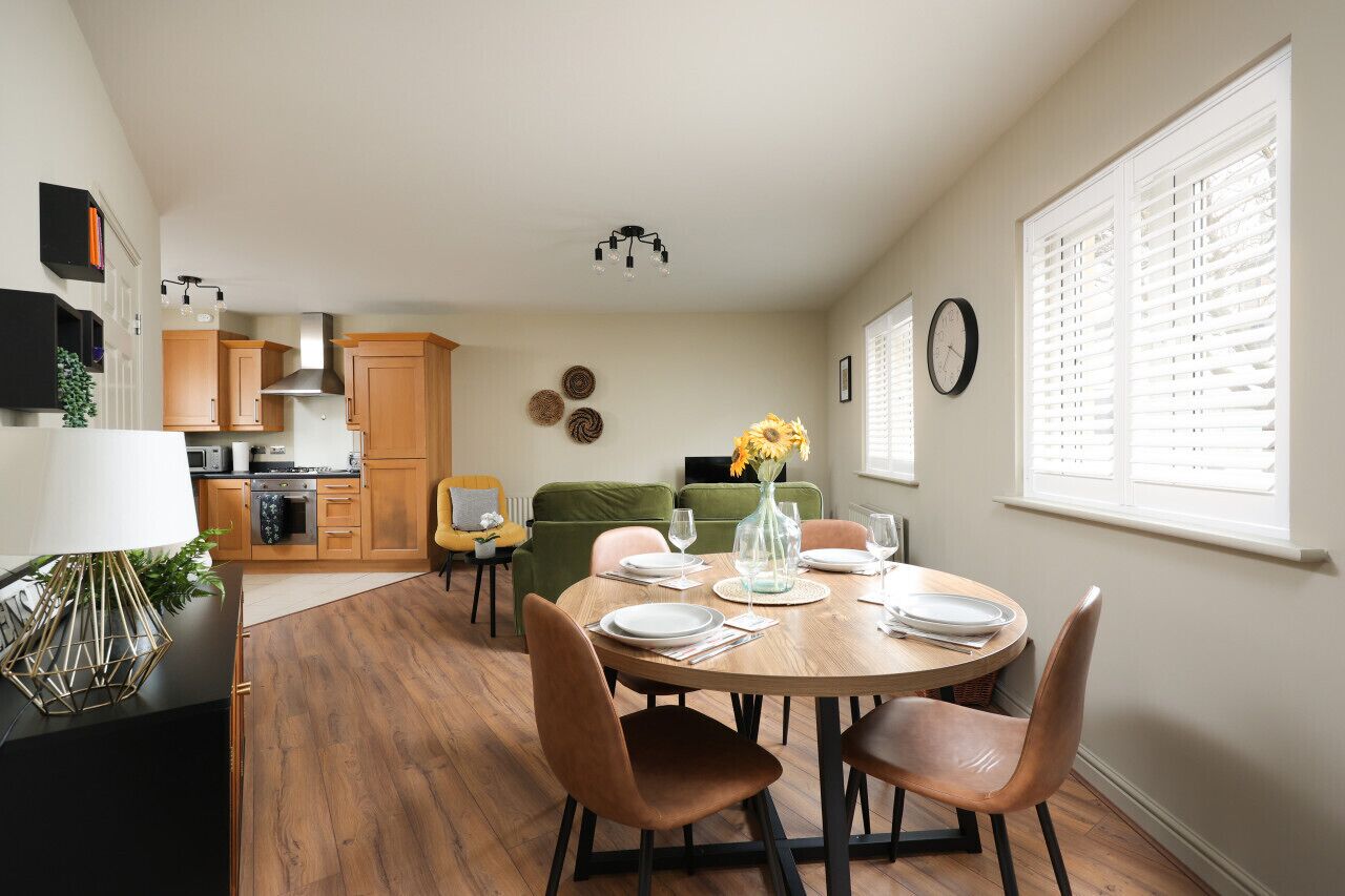 Cocina moderna con armarios de madera, una mesa de comedor para cuatro comensales y un sofá verde al fondo.