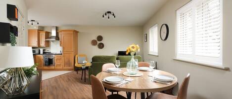 Cocina moderna con armarios de madera, una mesa de comedor para cuatro comensales y un sofá verde al fondo.