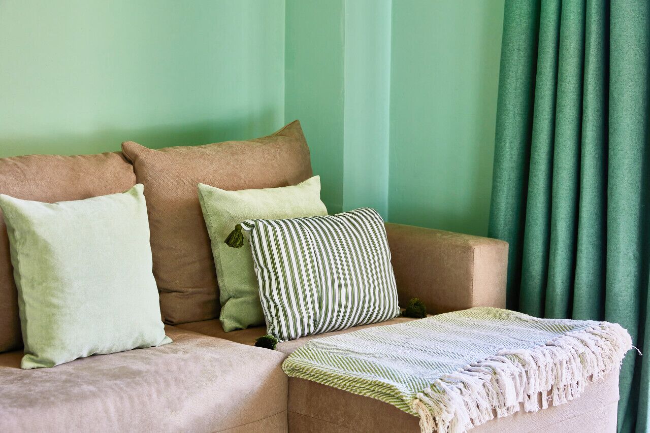 A beige sofa with three pillows, a striped pillow, and a woven throw blanket.