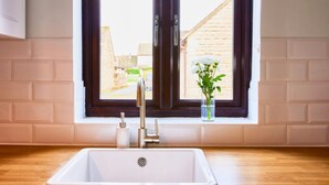 A kitchen with a white sink, a window with dark curtains, and a small vase with flowers on the windowsill.