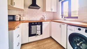 A compact kitchen with white cabinets, a black range hood, a built-in oven, a washing machine, and a window with a view.