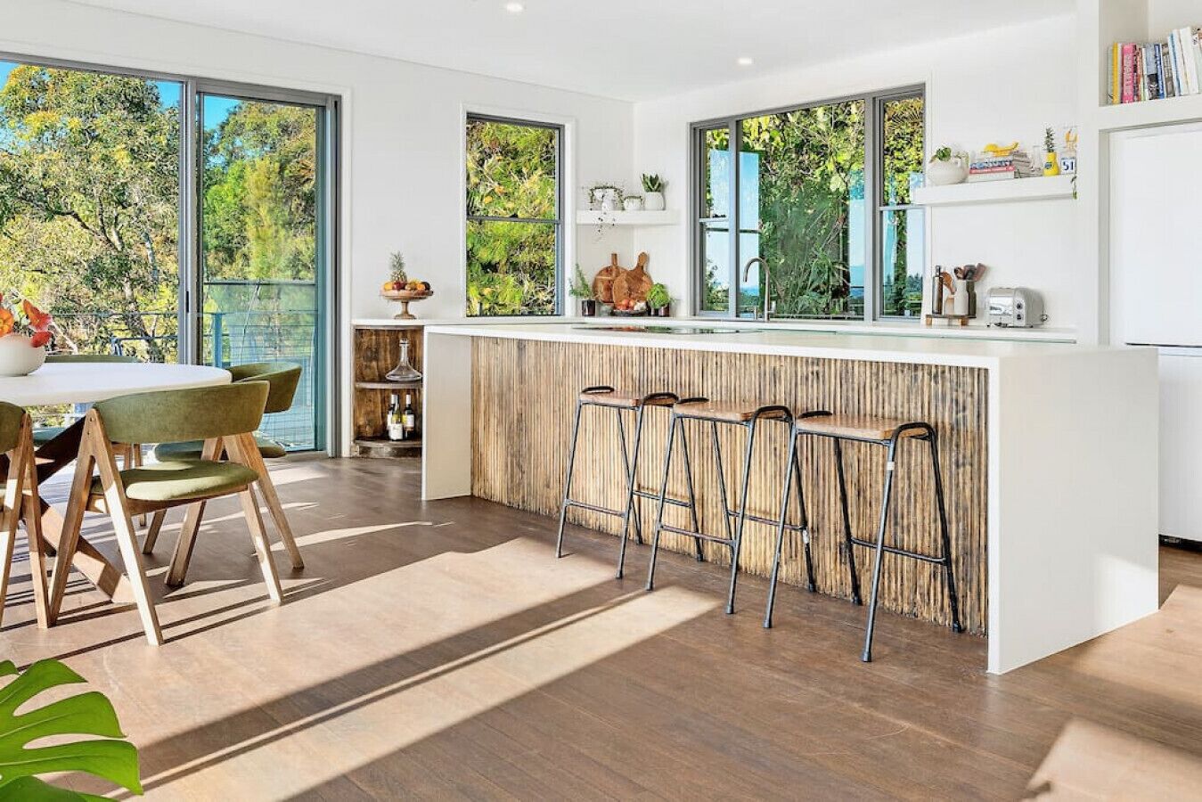 Een moderne keuken met een bar, grote ramen en een eethoek met een tafel en stoelen.