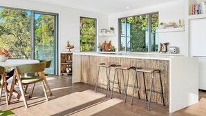 Et moderne køkken med barområde, store vinduer og et spiseområde med bord og stole.