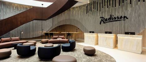 A modern lobby with a curved reception desk, multiple seating areas, and a large wall with vertical lines and the name 'Radisson'.