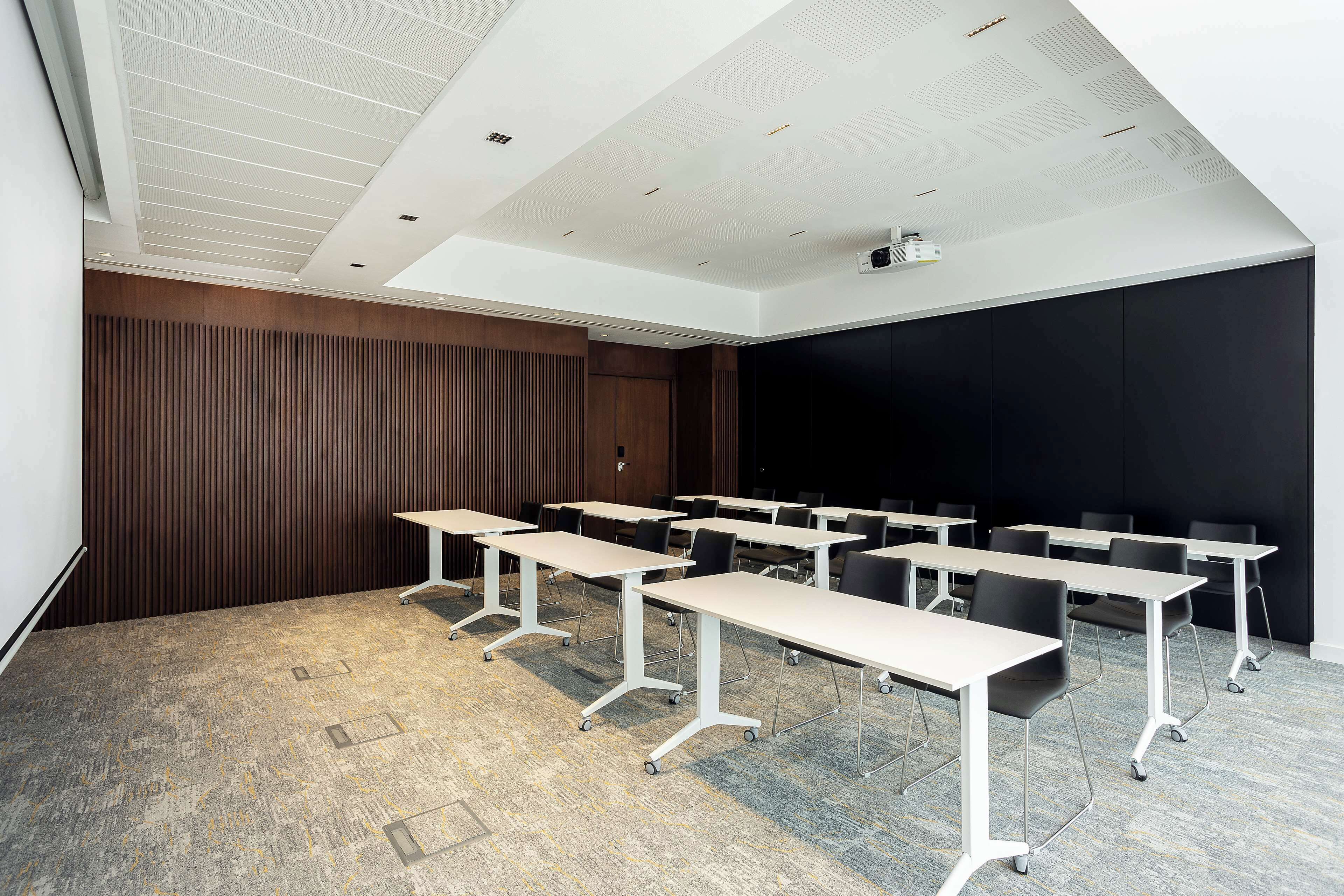 Une salle de conférence équipée de plusieurs tables et chaises, d’un projecteur et d’un grand écran.