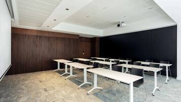 Une salle de conférence équipée de plusieurs tables et chaises, d’un projecteur et d’un grand écran.