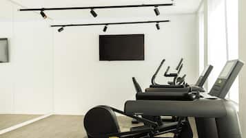 Une salle de sport équipée de matériel d’exercice, d’un téléviseur fixé au mur et d’une grande fenêtre laissant entrer la lumière naturelle.