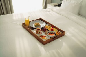 A neatly made breakfast tray on a bed with a variety of food items and a glass of orange juice. - Radisson Hotel Tunis, City Center (Tunis)