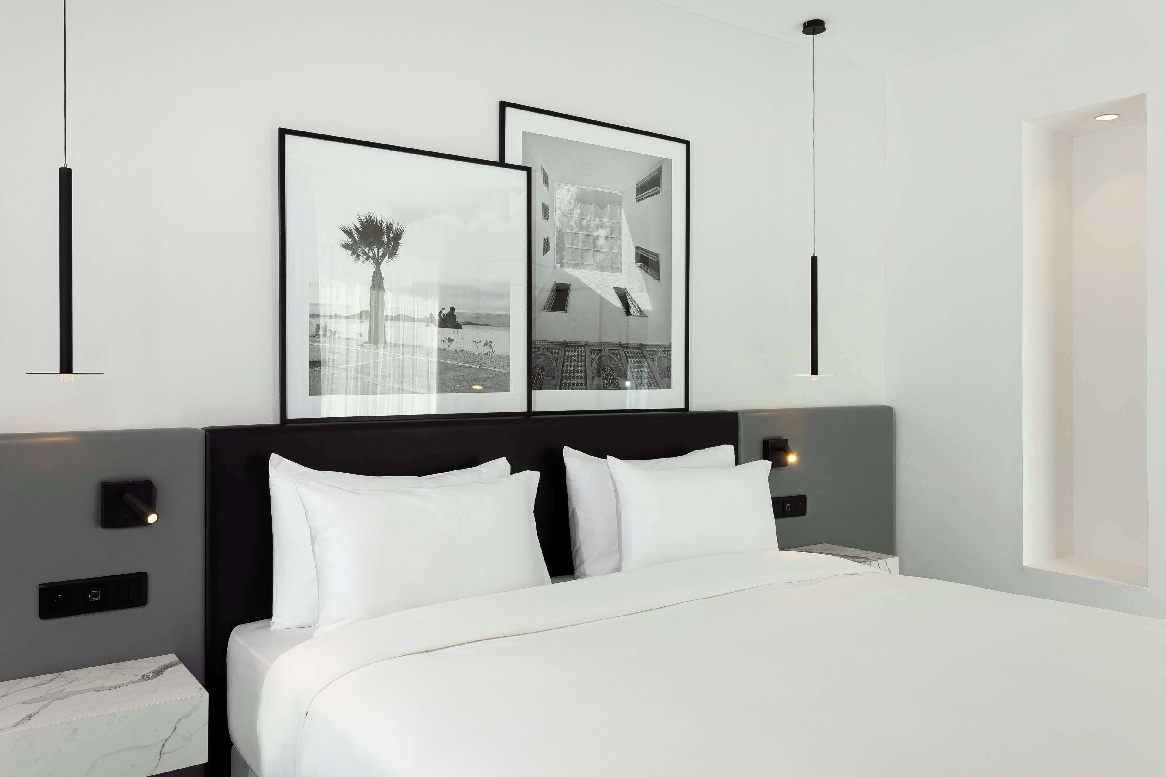 A modern hotel room with a large bed, a headboard with built-in lighting, and two framed pictures on the wall.