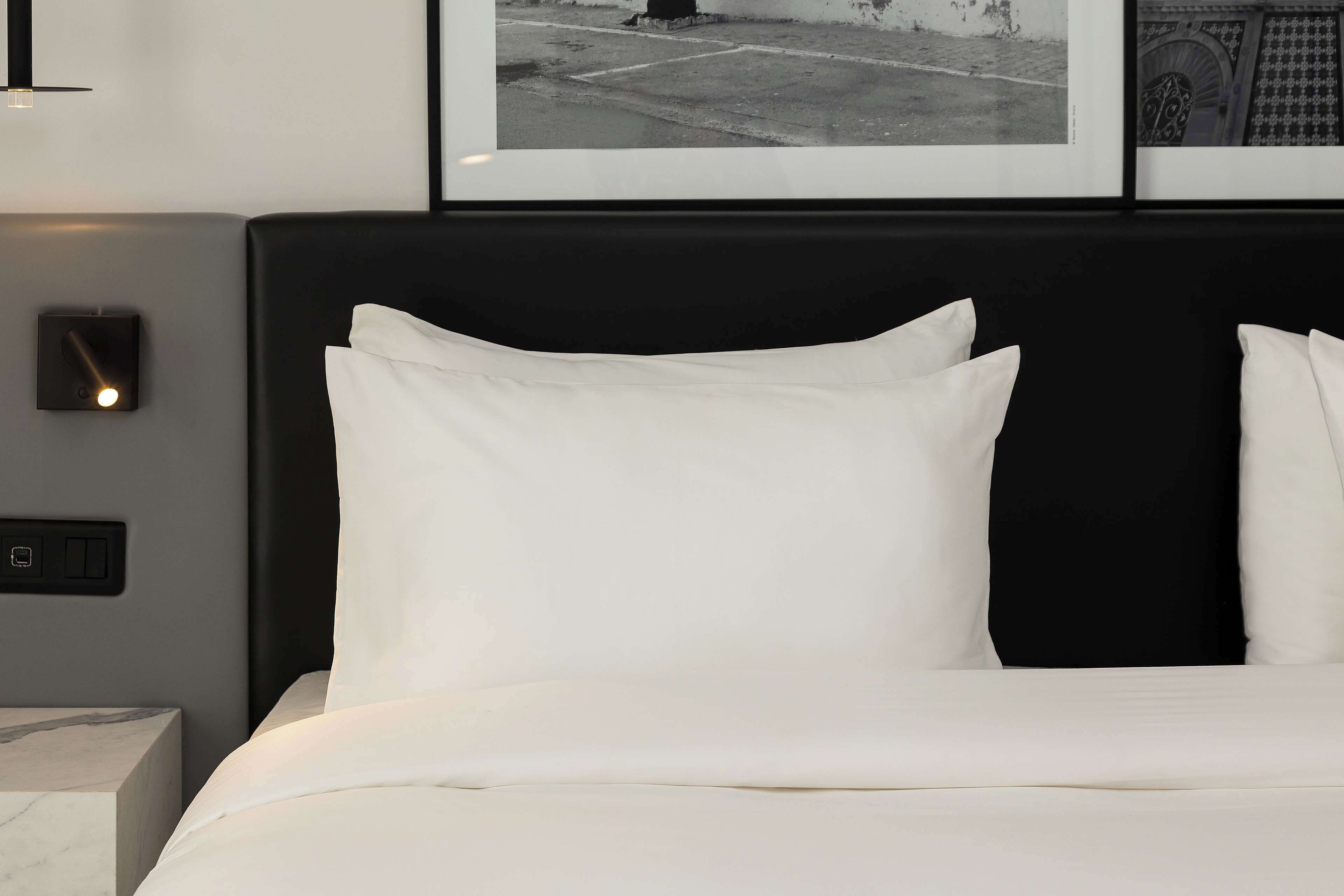 A neatly made bed with white linens and a black headboard.
