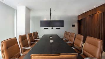 Una sala de conferencias con una mesa larga, sillas de cuero marrón, un televisor de pantalla plana y un diseño de techo moderno.
