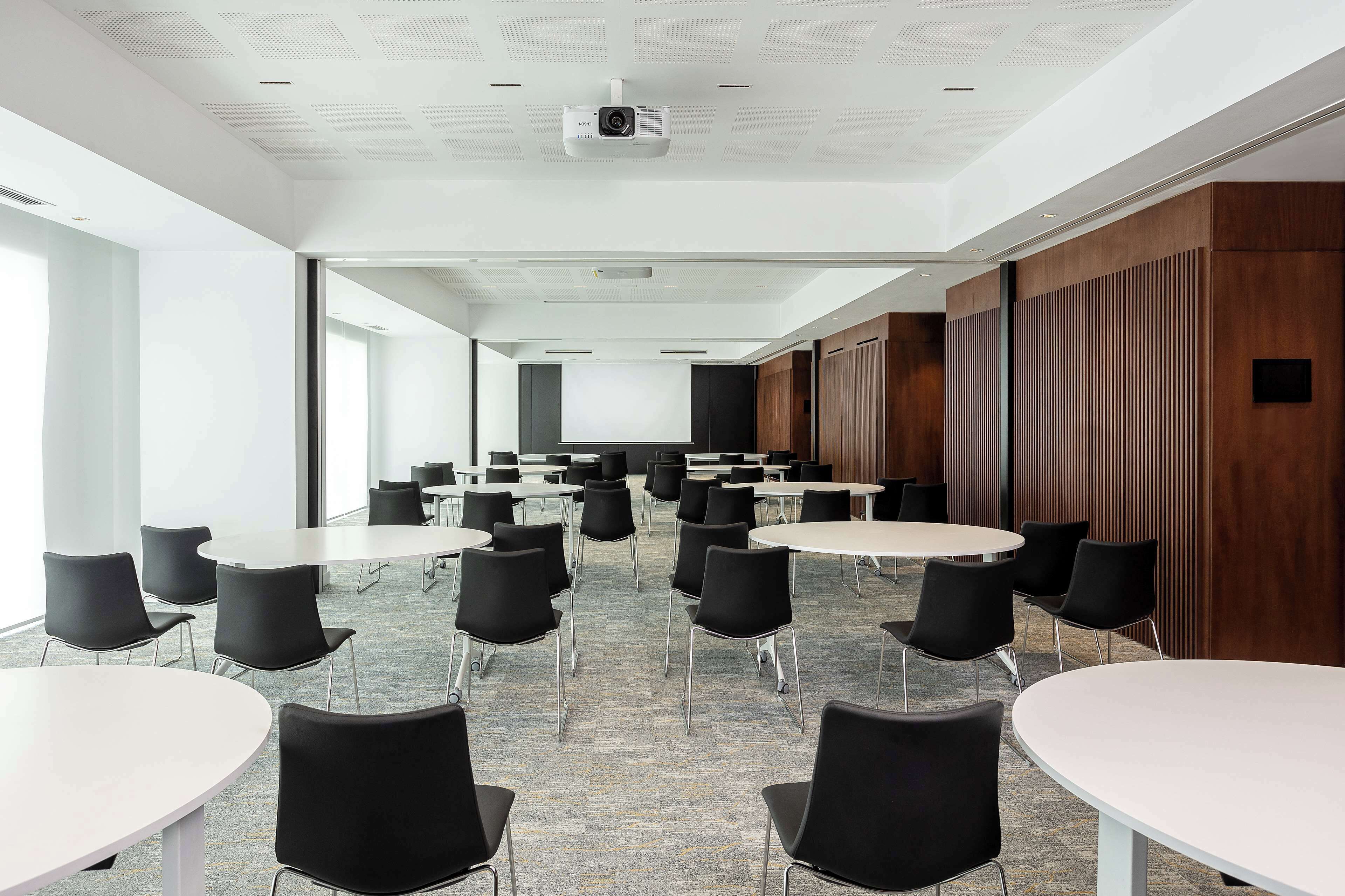 Una sala conferenze con diversi tavoli e sedie, un proiettore e uno schermo grande.