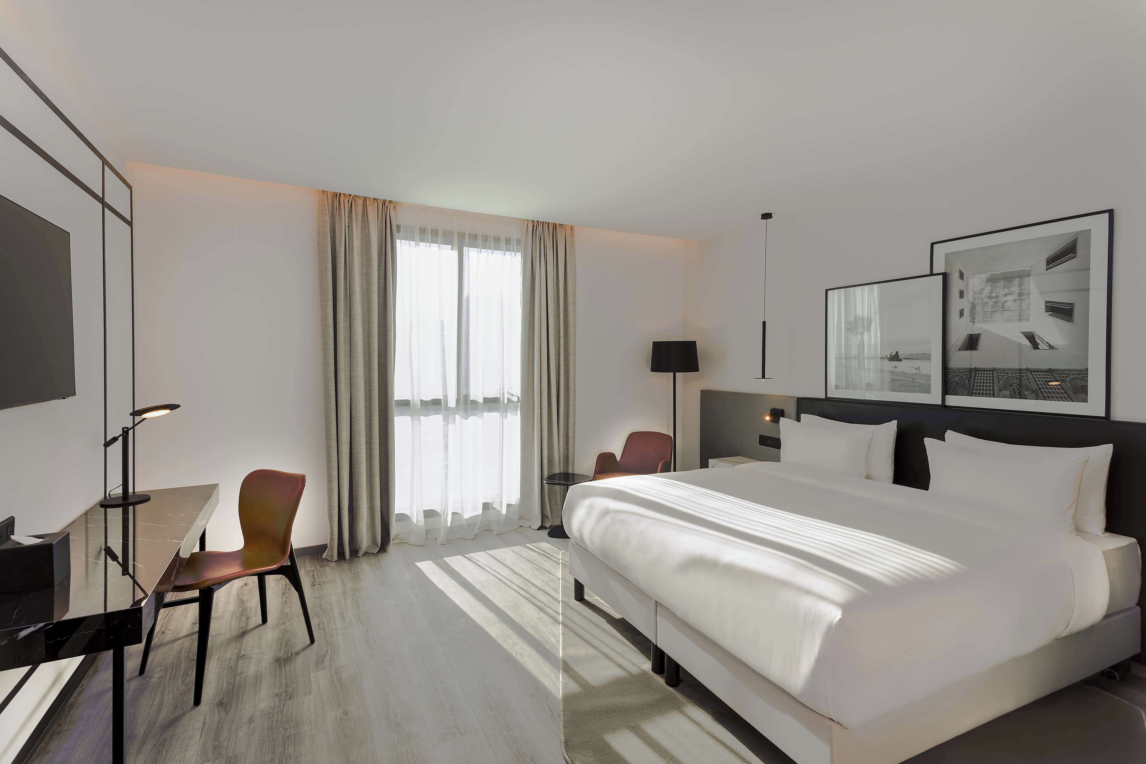 A hotel room with a large bed, a desk, a chair, and a window with curtains.