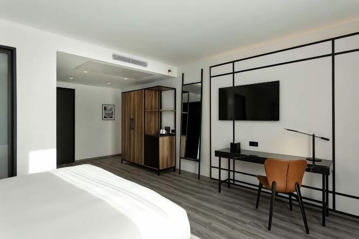 Ein modernes Hotelzimmer mit Bett, Schreibtisch, Stuhl, Kleiderschrank und Flachbildfernseher.