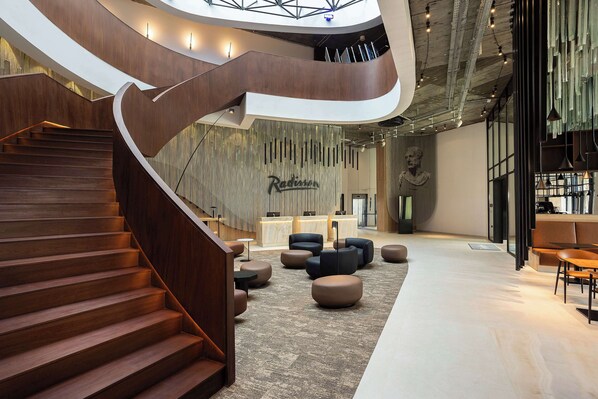 A modern lobby with a curved wooden staircase, comfortable seating areas, and a reception desk.