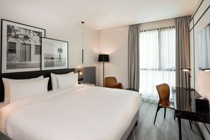 A modern hotel room with a large bed, a desk, and a chair. There are framed pictures on the wall and a lamp on the desk. - Radisson Hotel Tunis, City Center (Tunis)