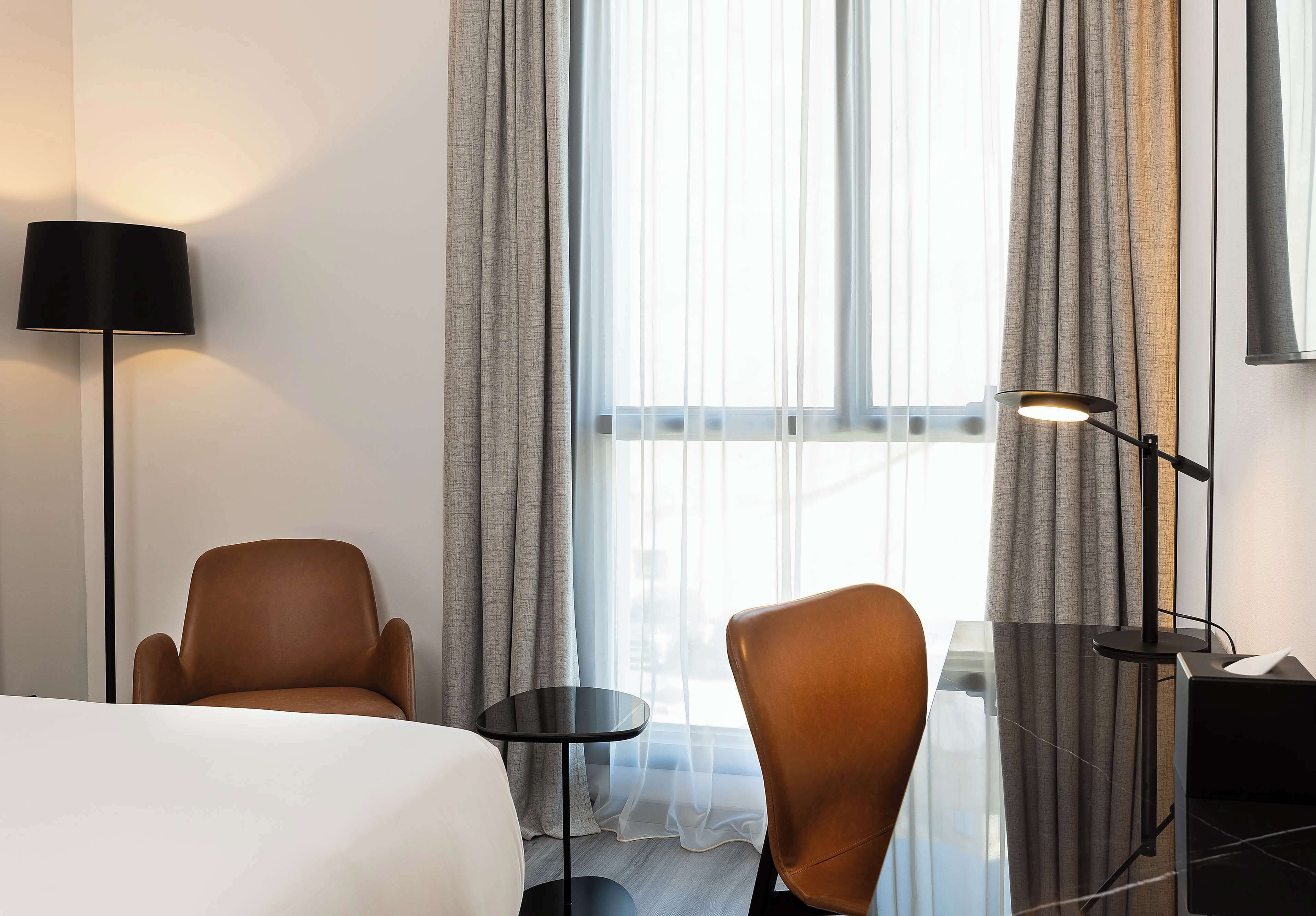 Habitación de hotel con cama, dos sillas, una mesita y una lámpara de pie.