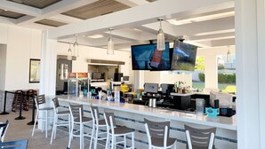 A modern bar area with a long counter, bar stools, and a television screen. - 1028L Resort 4BR Pool House FREE Grill by Disney (Kissimmee)