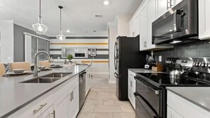 A modern kitchen with stainless steel appliances, a central island, and a striped backsplash. - 1028L Resort 4BR Pool House FREE Grill by Disney (Kissimmee)