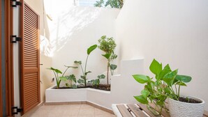 A small, enclosed patio area with tiled flooring, wooden benches, and potted plants. - Blue Jasmine II (Chania)