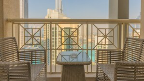 Un balcón con mobiliario de mimbre y una mesa de vidrio, con vistas a un paisaje urbano de edificios altos.