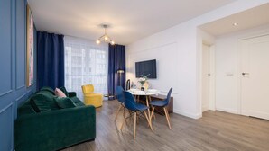 Un salon moderne avec un canapé vert, un fauteuil jaune et un coin repas comprenant des chaises bleues et une table blanche.