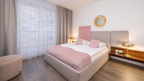 Une chambre d’hôtel moderne avec un grand lit, une table de chevet avec une lampe, une petite table d’appoint et une vue sur la ville grâce à de grandes fenêtres.