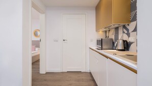 Une cuisine moderne avec des meubles blancs, un plan de travail en bois et une bouilloire en acier inoxydable.