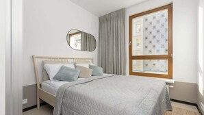 A bedroom with a bed, a window with curtains, a mirror, and a wall with a geometric pattern. - Stylish Apartment in the Center | Air Conditioning and Balcony (Warszawa)