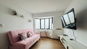 Ein modernes Wohnzimmer mit einem rosafarbenen Sofa, einem flachbildfernseher an der Wand und einem großen Fenster, das für natürliches Licht sorgt.