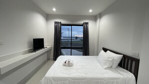 Una habitación de hotel con cama, televisor en un estante y ventana con cortinas.