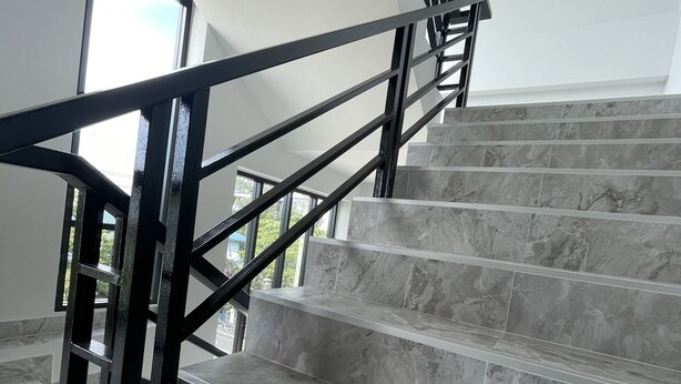 Una escalera con barandillas de metal negro y peldaños de mármol gris.