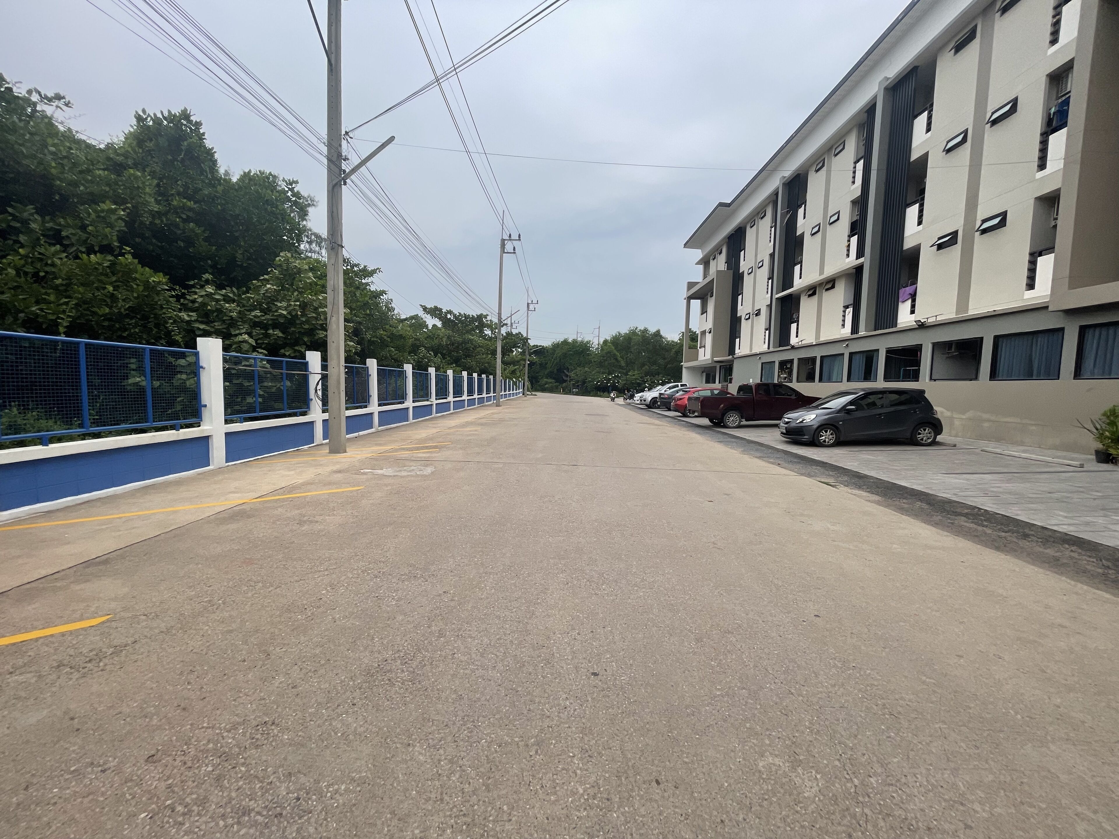 A parking area with cars, a blue fence, and a building with multiple windows.