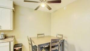 A small dining area with a table and four chairs, a ceiling fan, and a trash bin.