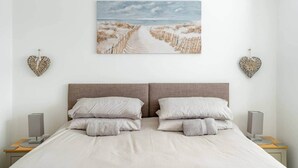 A bedroom with a large bed, two heart-shaped wall decorations, a painting of a beach, and a bedside table with a lamp.