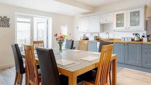A modern kitchen with white cabinets, a dining area with a wooden table and chairs, and a vase of flowers on the table.