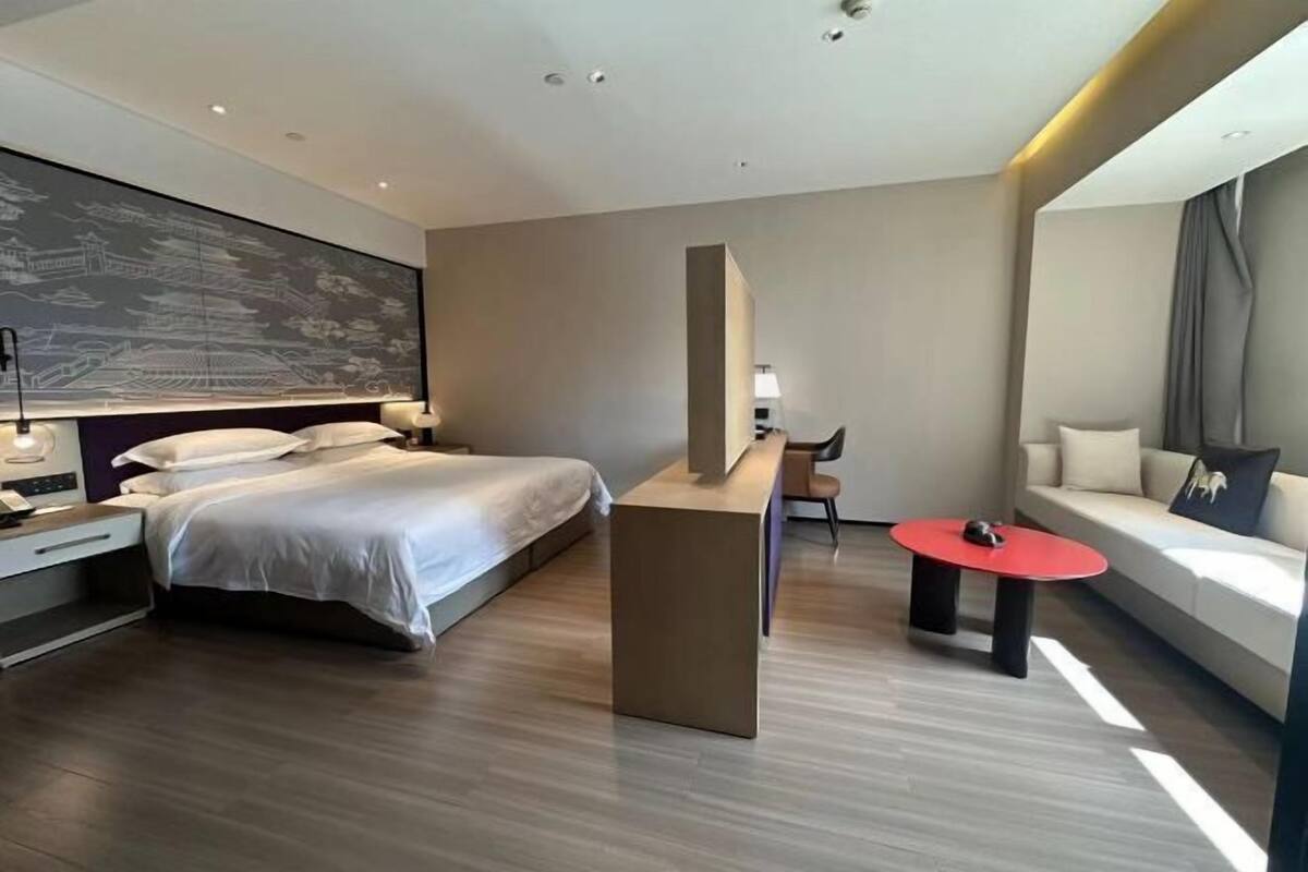 Et moderne hotelværelse med seng, skrivebord, et rødt bord og en sofa.