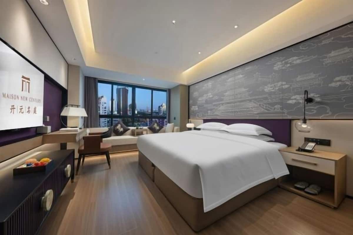 Et moderne hotelværelse med en stor seng, udsigt over byen, et skrivebord med lampe og et fjernsyn.