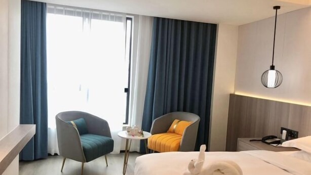 A hotel room with a bed, two chairs, a small table, a nightstand with a phone, and a window with curtains. - Maison New Century Hotel Wucheng Jinhua (Jinhua)