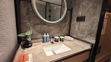 A bathroom with a marble sink, a round mirror, toiletries, and a potted plant.