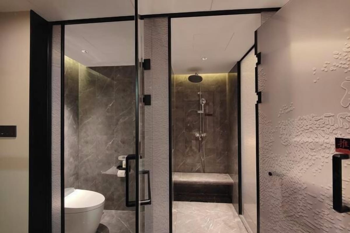 A modern bathroom with a glass partition, a toilet, a shower area, and a textured wall.