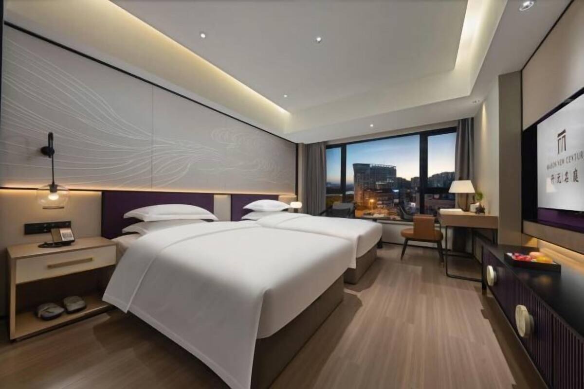 Et moderne hotelværelse med to senge, et skrivebord, en stol, et fjernsyn og udsigt over byen.