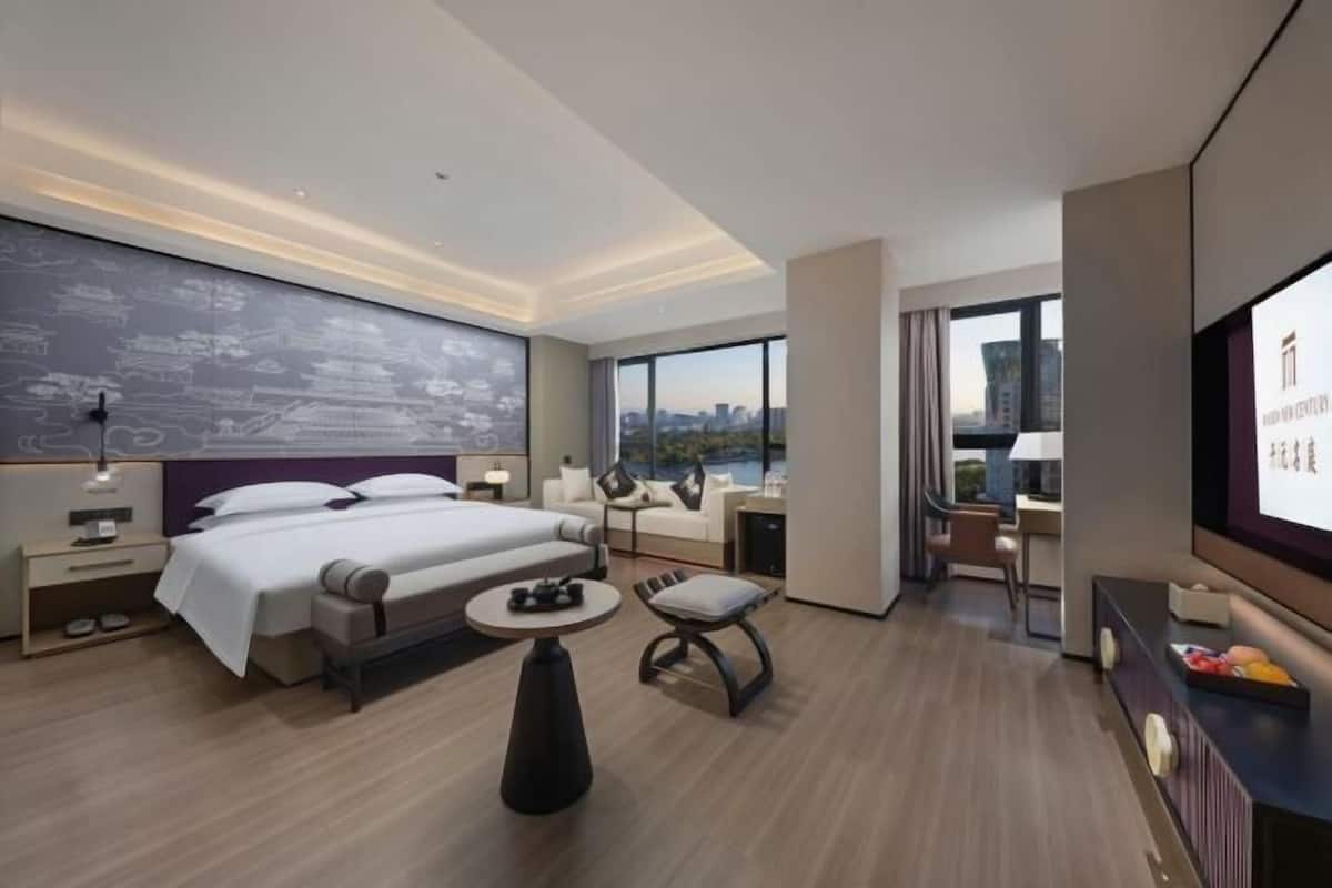 Et moderne hotelværelse med en stor seng, et skrivebord, en stol og et fjernsyn.