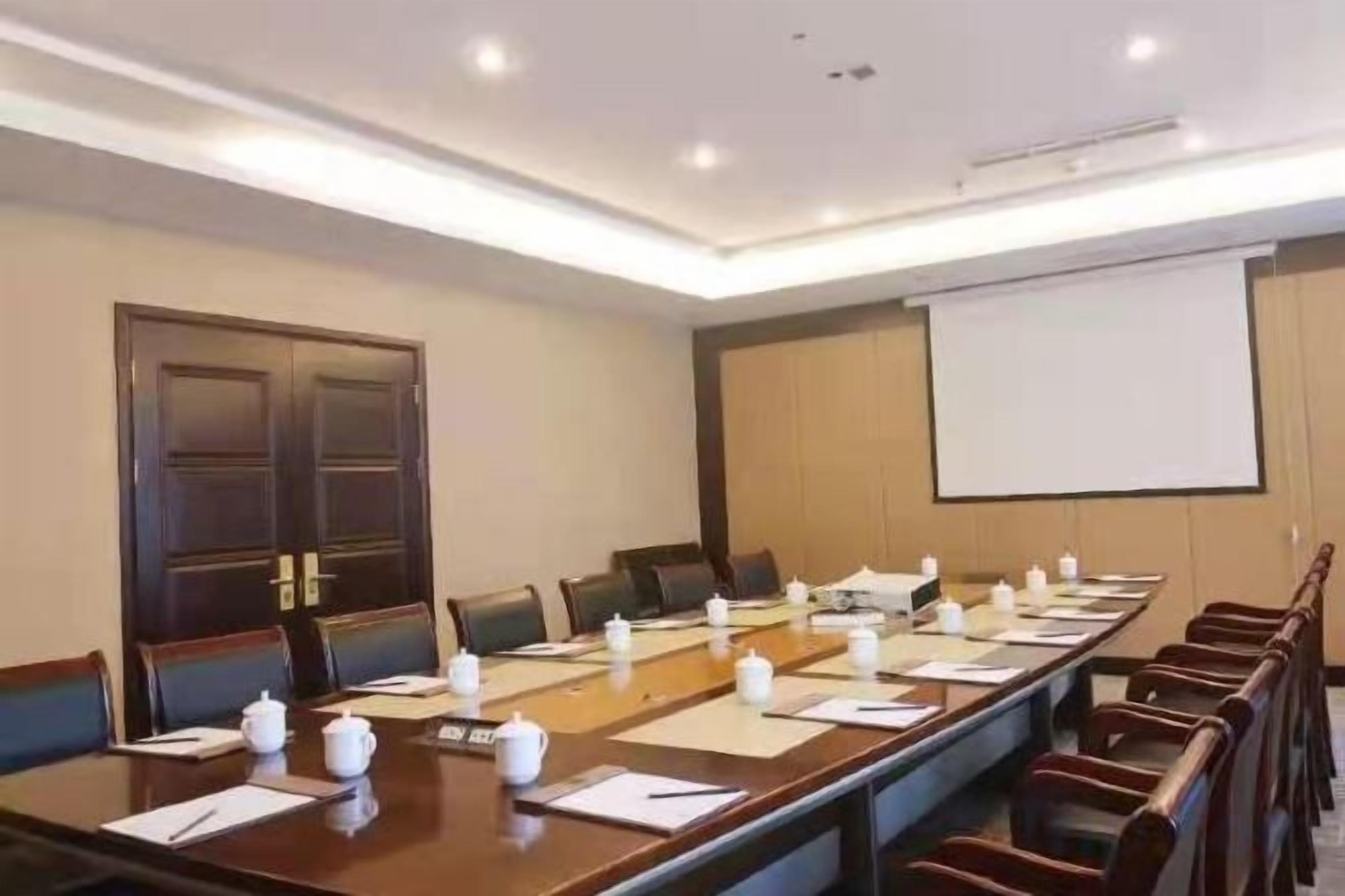 A conference room with a long table, chairs, a projector screen, and a whiteboard.