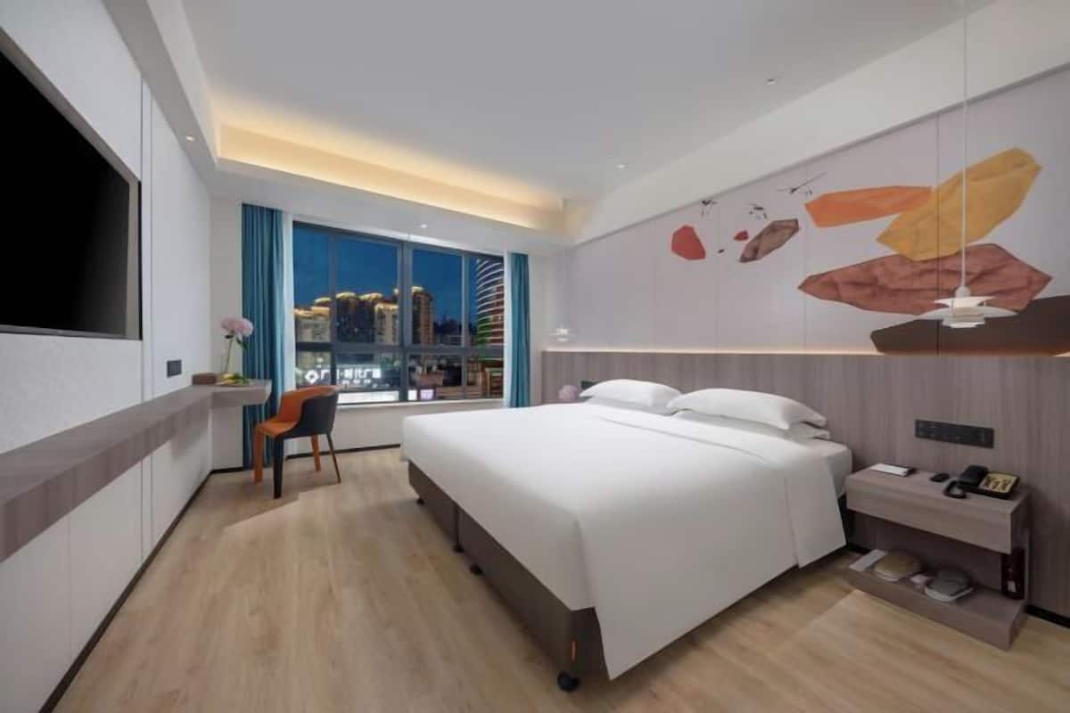 Et moderne hotelværelse med en stor seng, et skrivebord, en stol, et fjernsyn og udsigt over byen.