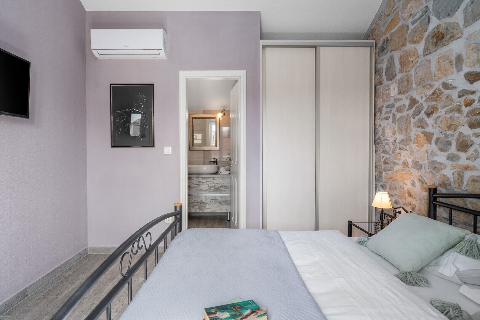 A bedroom with a bed, bedside tables, a TV, and an air conditioning unit.