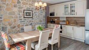 Une cuisine avec des murs en pierre, des meubles de rangement en bois, une table à manger avec des chaises et un banc coloré.